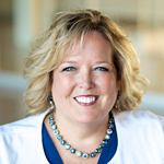 M. Gayle Packer in a blue dress and white blazer with necklace