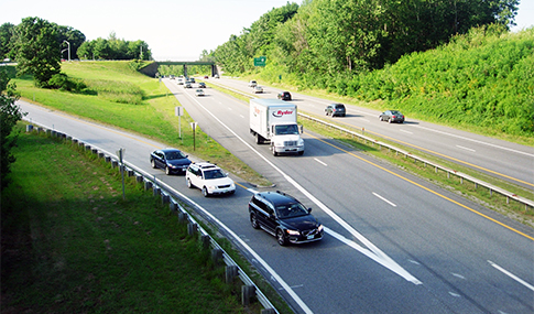 Three cars merge onto an interstate in front of a truck.