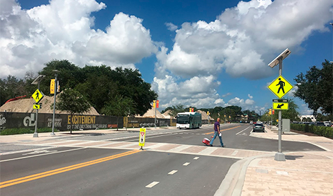 Man in the middle of a street crosswalk, with yellow signs and an oncoming bus in the other lane. 