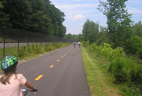 People ride bicycles along a trail next to railroad tracks.