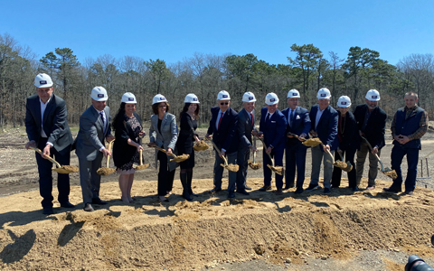 People in hardhats with shovels on a mound of dirt. 