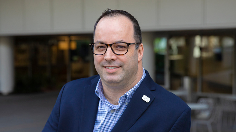 Dave Mulholland wearing glasses, a blue collared shirt and a jacket