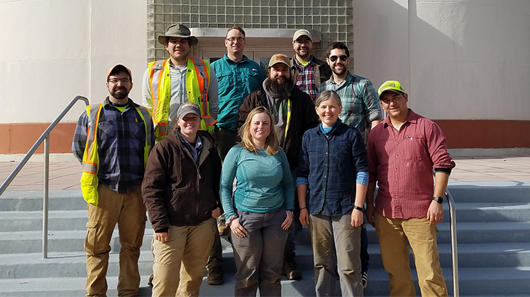 A team of archaeologists stand on the steps of a National Park Service building