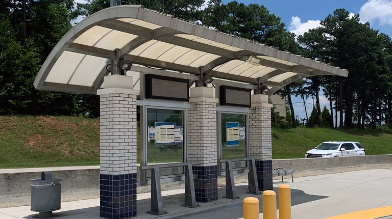 A photo of a modern covered bus stop with shade and maps for riders. 