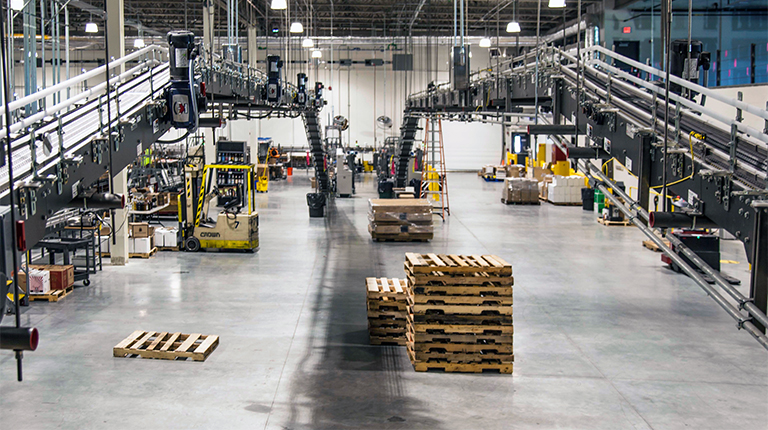 Pallets are stacked and automated machinery is shown centered inside a large industrial distribution warehouse