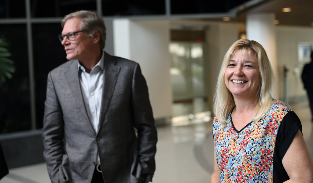 A smiling woman and man stand together in an office setting.