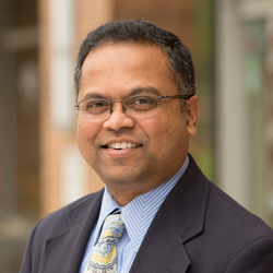 Vinod Kalikiri wearing a dark suit and printed yellow tie.