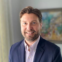 A business headshot of a man with brown hair wearing a buttoned shirt and blue jacket.