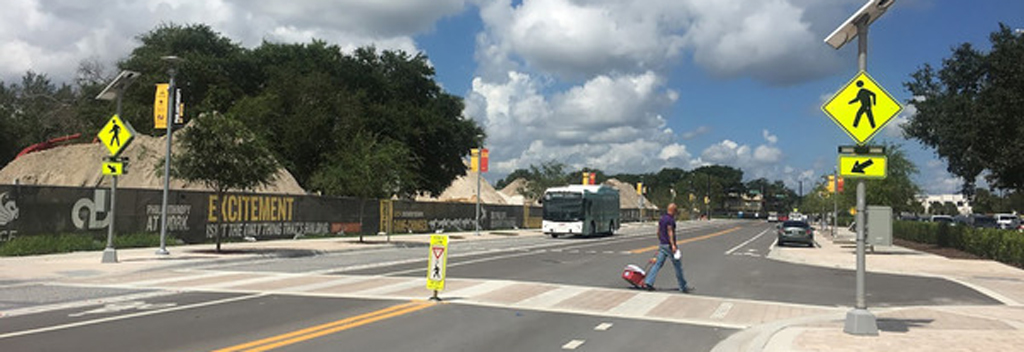 A crosswalk on a busy street, with security cameras and safety signs